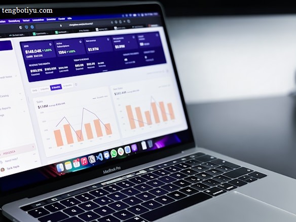 A laptop with an open screen displaying dashboard analytics featuring charts, graphs, and numerical data related to sales and subscriptions. The interface is predominantly dark-themed with sections highlighting key performance metrics. The device shown is a MacBook Pro, indicated by the keyboard layout and branding.
